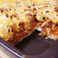 deep dish taco casserole with seasoned turkey, cheese, refried beans, and taco rice on pizza crust