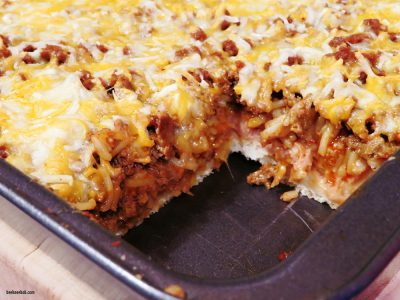 deep dish taco casserole with seasoned turkey, cheese, refried beans, and taco rice on pizza crust