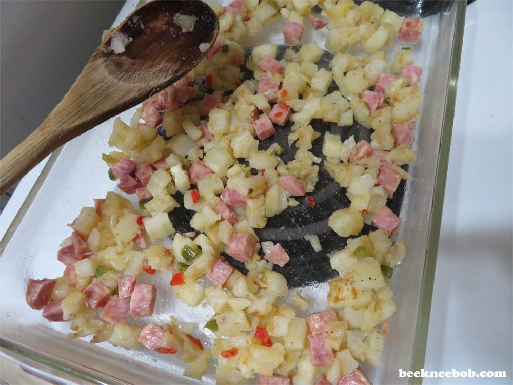 layer of hash brown potatoes, peppers, onions, and diced ham in breakfast casserole dish