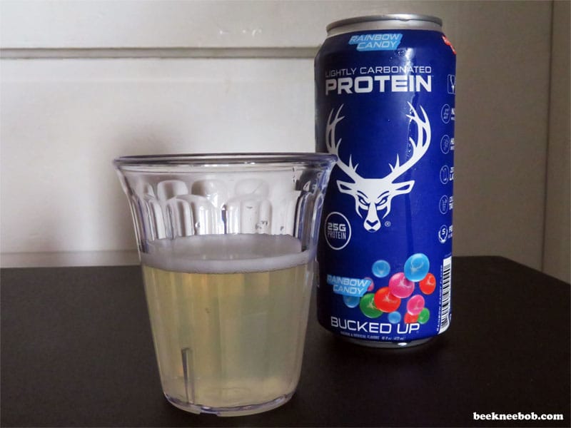 Bucked Up Rainbow Candy Protein Soda can next to a glass of the poured, clear soda.