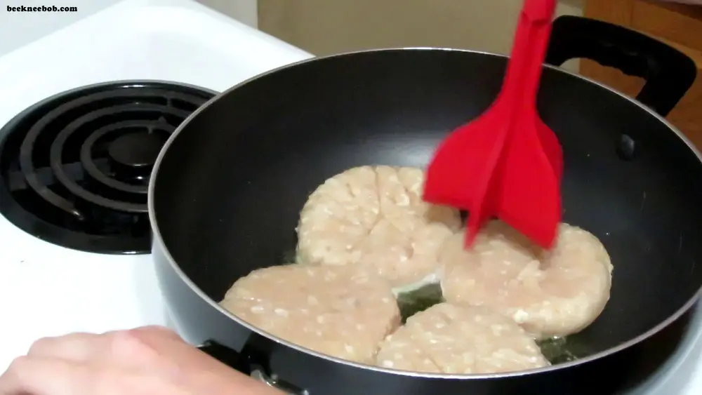 four raw chicken patties in a skillet with a meat masher