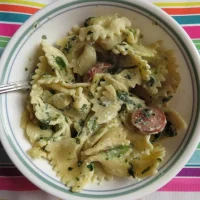 Close-up of a single serving bowl of leftover pasta containing bowtie noodles, Alfredo sauce, spinach, and smoked sausage.