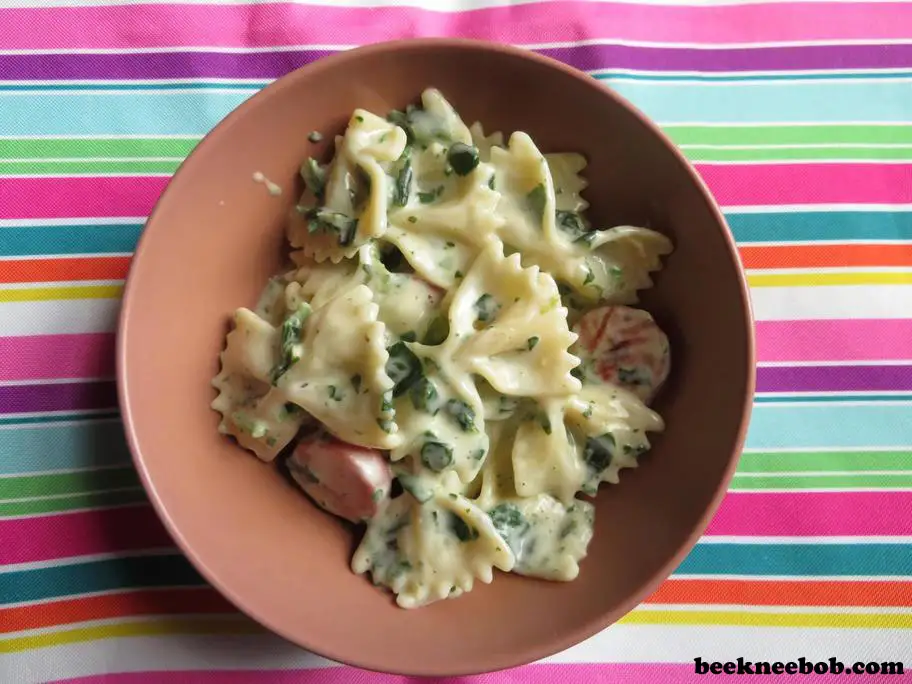 A single serving bowl of creamy smoked sausage and spinach bowtie pasta in Alfredo sauce on a multicolored striped place mat.