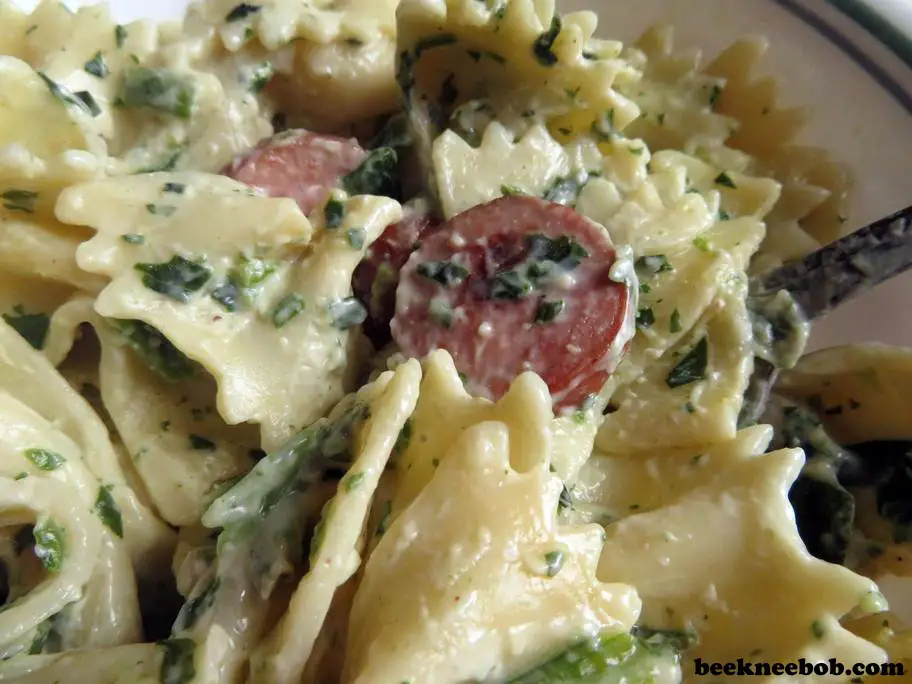 A close-up of a bowl of creamy smoked sausage and spinach pasta featuring bowtie noodles.
