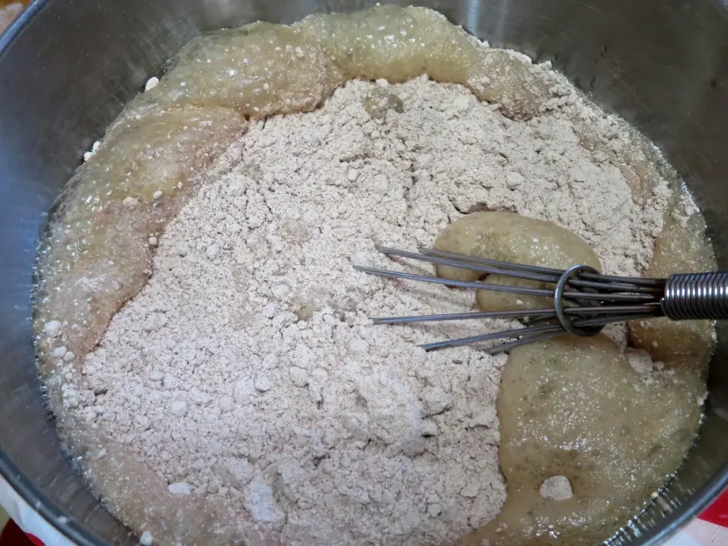 A bowl of dry German chocolate cake mix added to cherry cola soda with a whisk, ready to mix into a cake batter