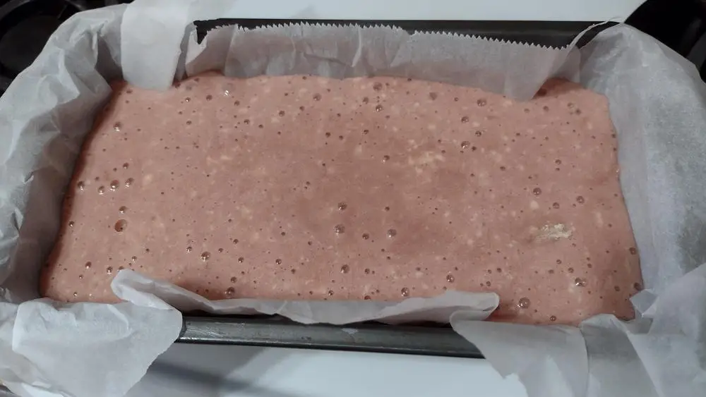 Prepared pink batter for dragon fruit quick bread in a loaf pan lined with parchment paper