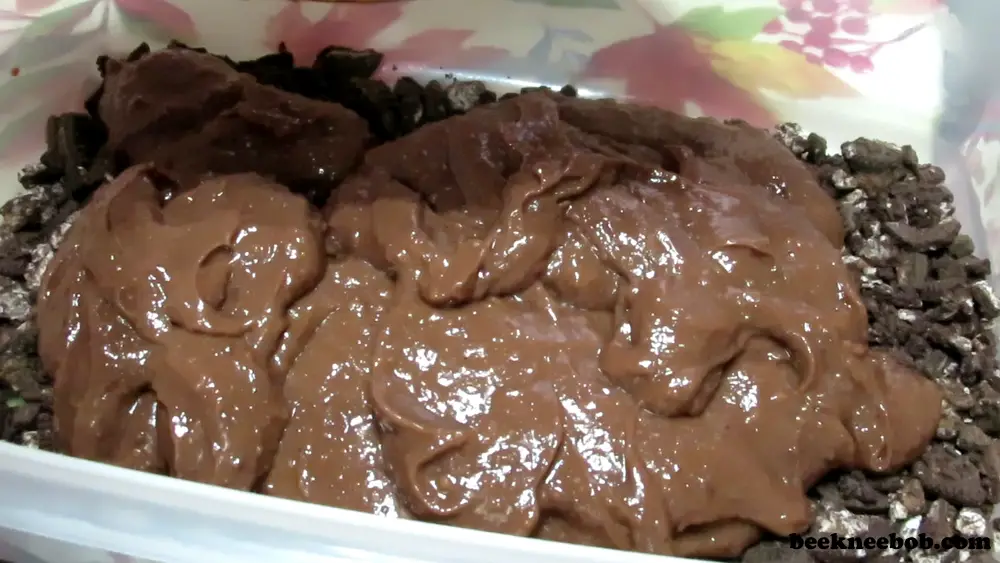 pouring chocolate vanilla pudding over a layer of crushed Oreo cookies as part of the peanut butter oreo dirt pudding dessert