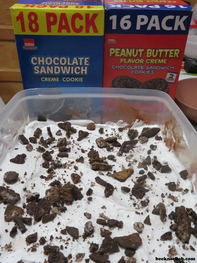 A completed peanut butter Oreo dirt pudding dessert with two boxes of Sobisk sandwich cookies standing behind it