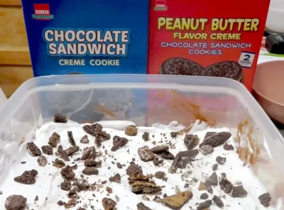 A completed peanut butter Oreo dirt pudding dessert with two boxes of Sobisk sandwich cookies standing behind it