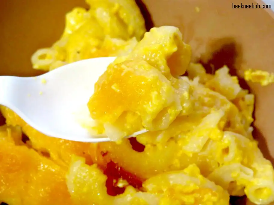 plastic spoon holding noodles over a bowl of baked macaroni and cheese