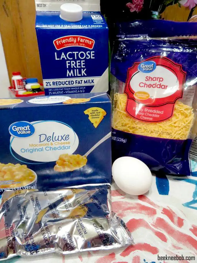 a layout of ingredients used in a 4-ingredient baked macaroni and cheese, including boxed pasta, shredded cheese, milk, and an egg
